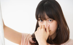 Young woman smelling stinky moldy, mildew laundry