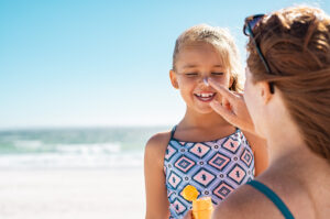 Woman hand putting sunscreen lotion on child face