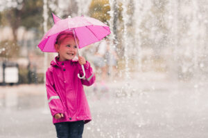 young girl wearing a pink raincoat and holding a pink umbrella