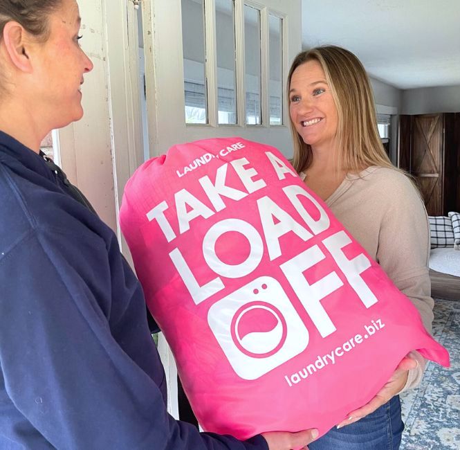 Laundry service provider standing at a customer's door while the customer hands over her pink bag of dirty laundry