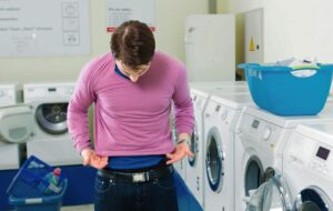 frustrated man putting a sweater on while noticing it has shrunk in the wash